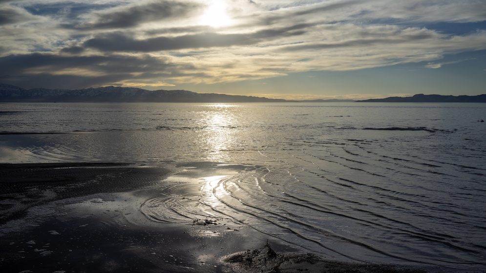 A body of water with a mountain in the background. The sunlight reflects off the water