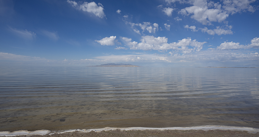 A sandy beach with a small island in the distance on clear water