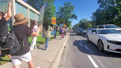 A group of people protesting on the sidewalk next to the street