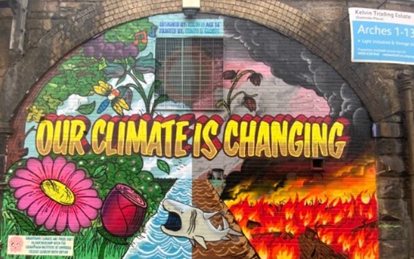 A mural of a green, thriving outdoor scene and a burning, desolate outdoor scene on a brick wall reading "Our climate is changing"
