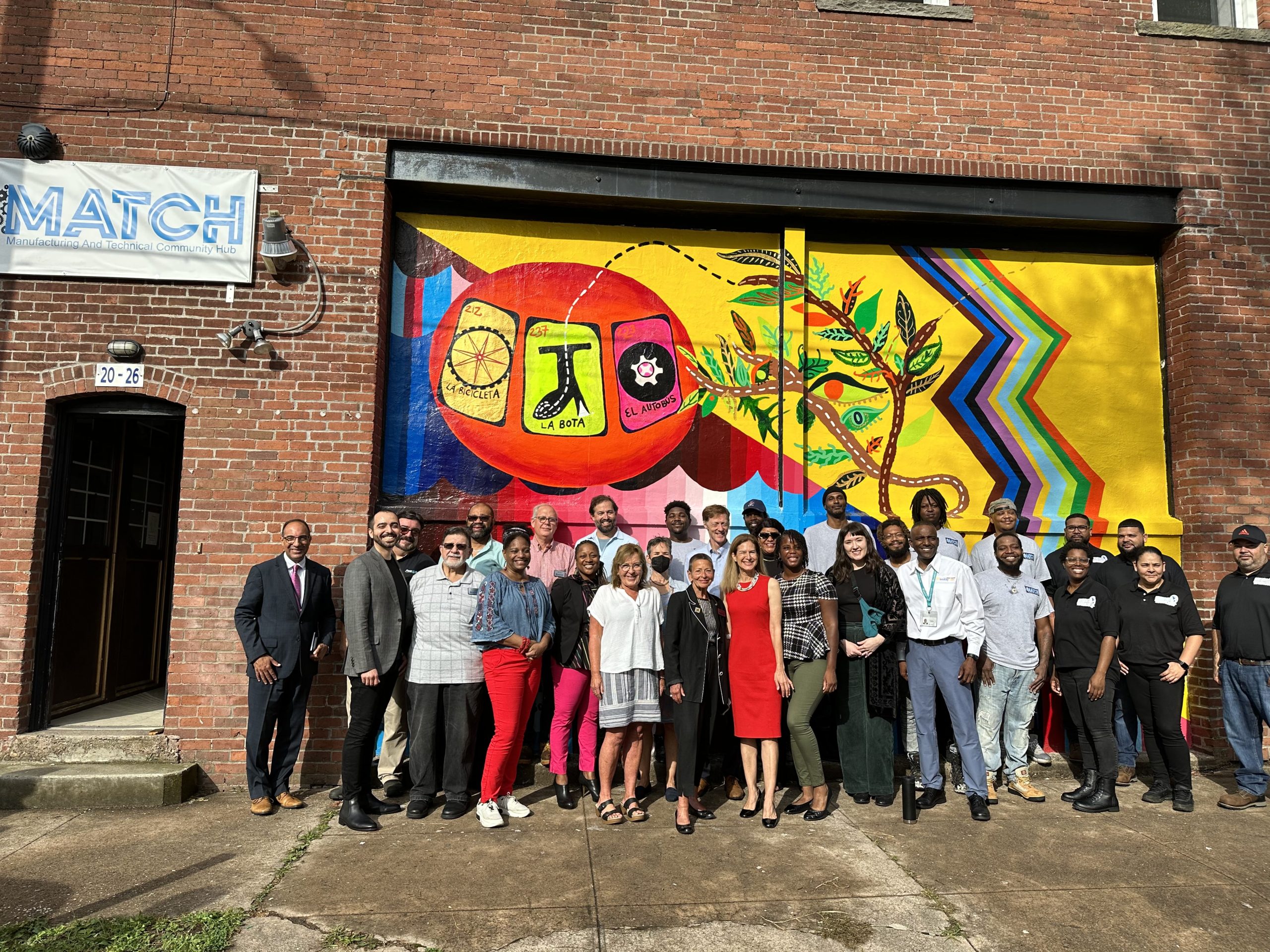 A group of people posing in front of a colorful mural depicting a tree's life cycle