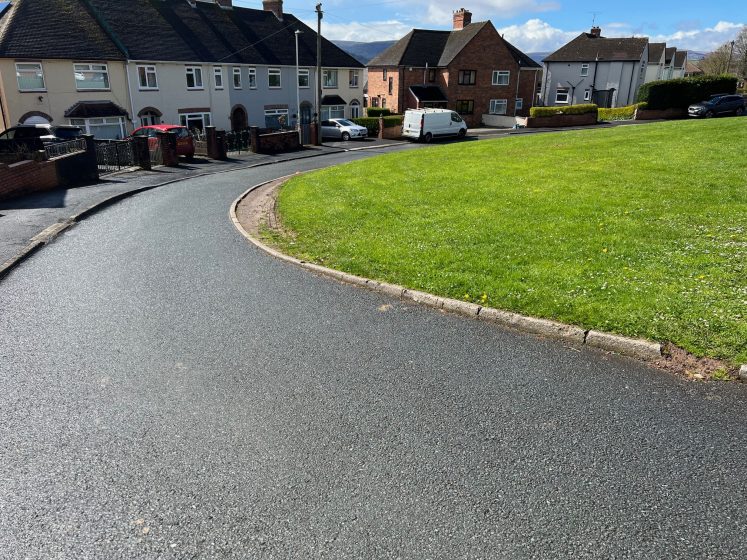 A paved cul-de-sac with green grass and buildings 