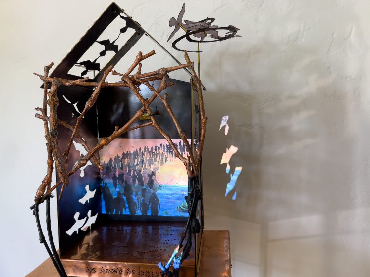 An art exhibit depicting a house made of dry wood, and paper birds flying around
