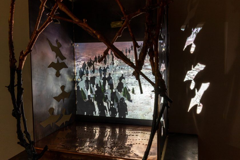 An darkened art exhibit depicting a house made of dry wood, and paper birds flying around