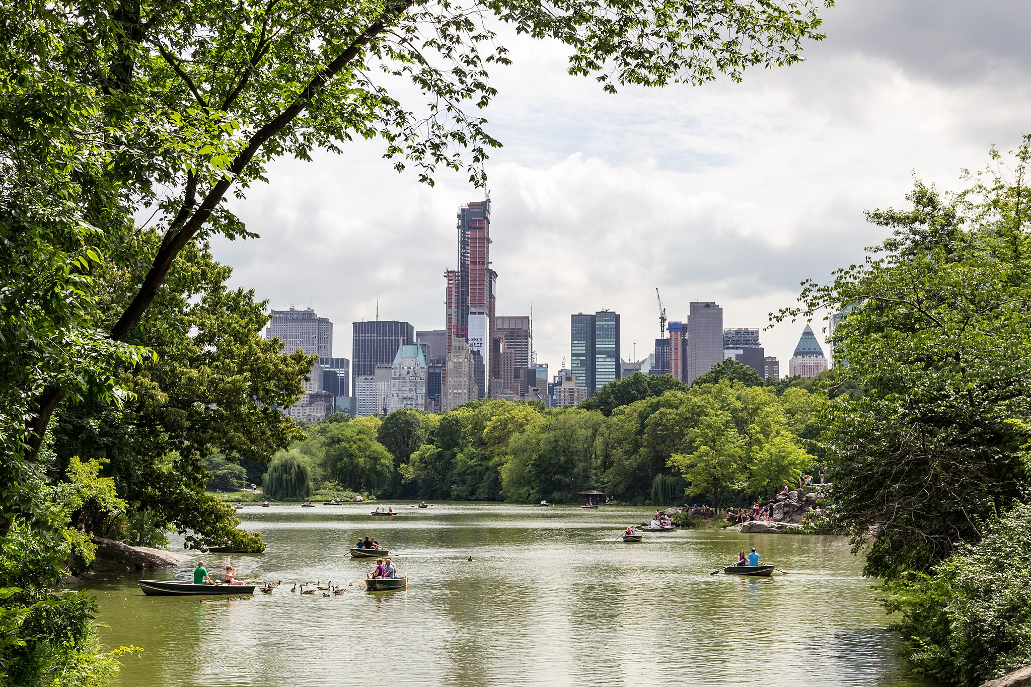 Central Park. A vast river with people kayaking, surrounded by green trees, and skyscrapers on the horizon