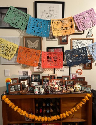 A table with an ofrenda with multiple photos, skulls, and flags
