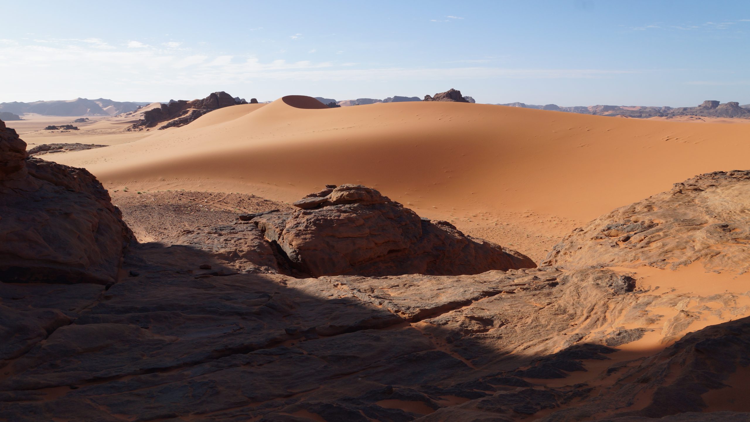 A vast landscape of red sand dunes and rocky hills