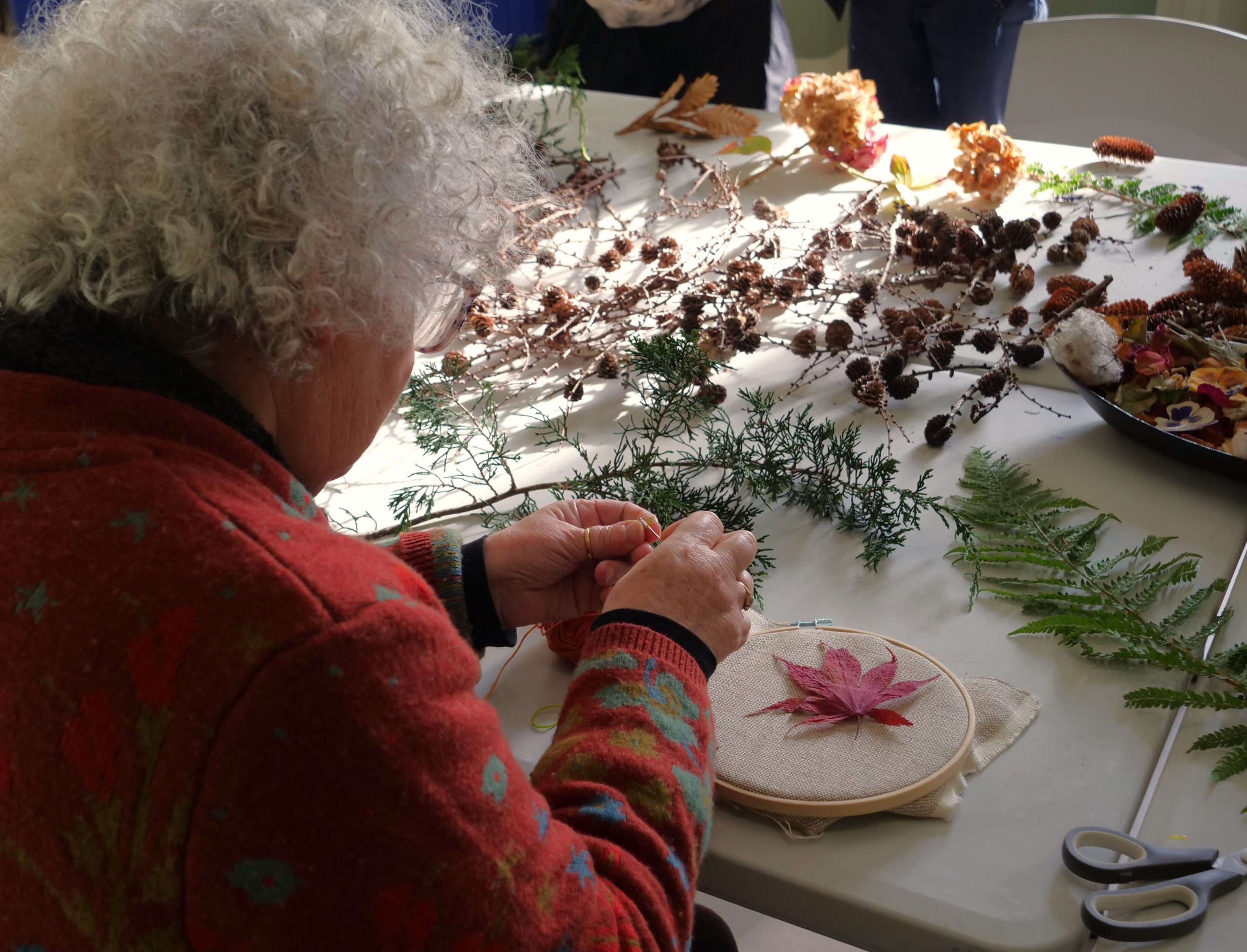 An older woman crafting at a table covered in dried flowers