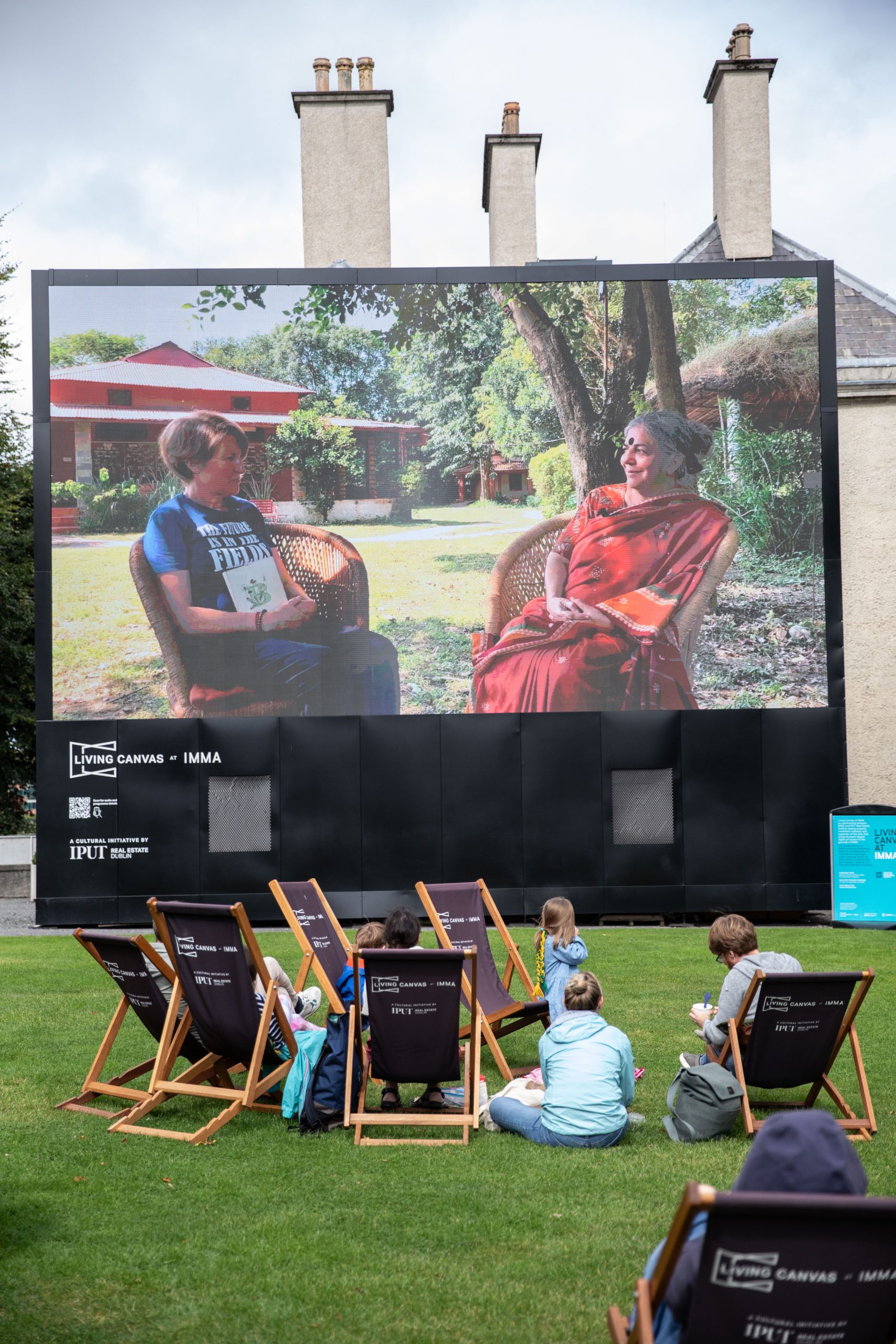 A group of people on a lawn watching a movie on a projection screen