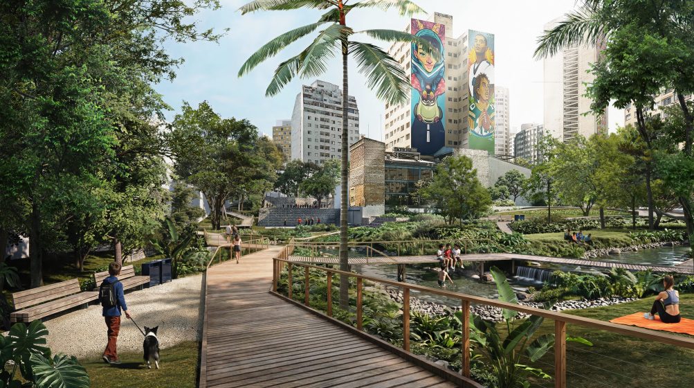 Photo of an urban park featuring a wooden boardwalk, gravel path, and lush greenery with people walking, sitting, and relaxing. Tall buildings with colorful murals are visible in the background