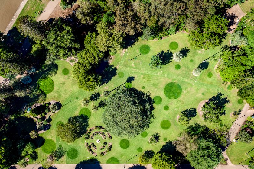 Aerial photo of a park showing various trees, pathways, and circular patches of darker grass scattered across a large green lawn
