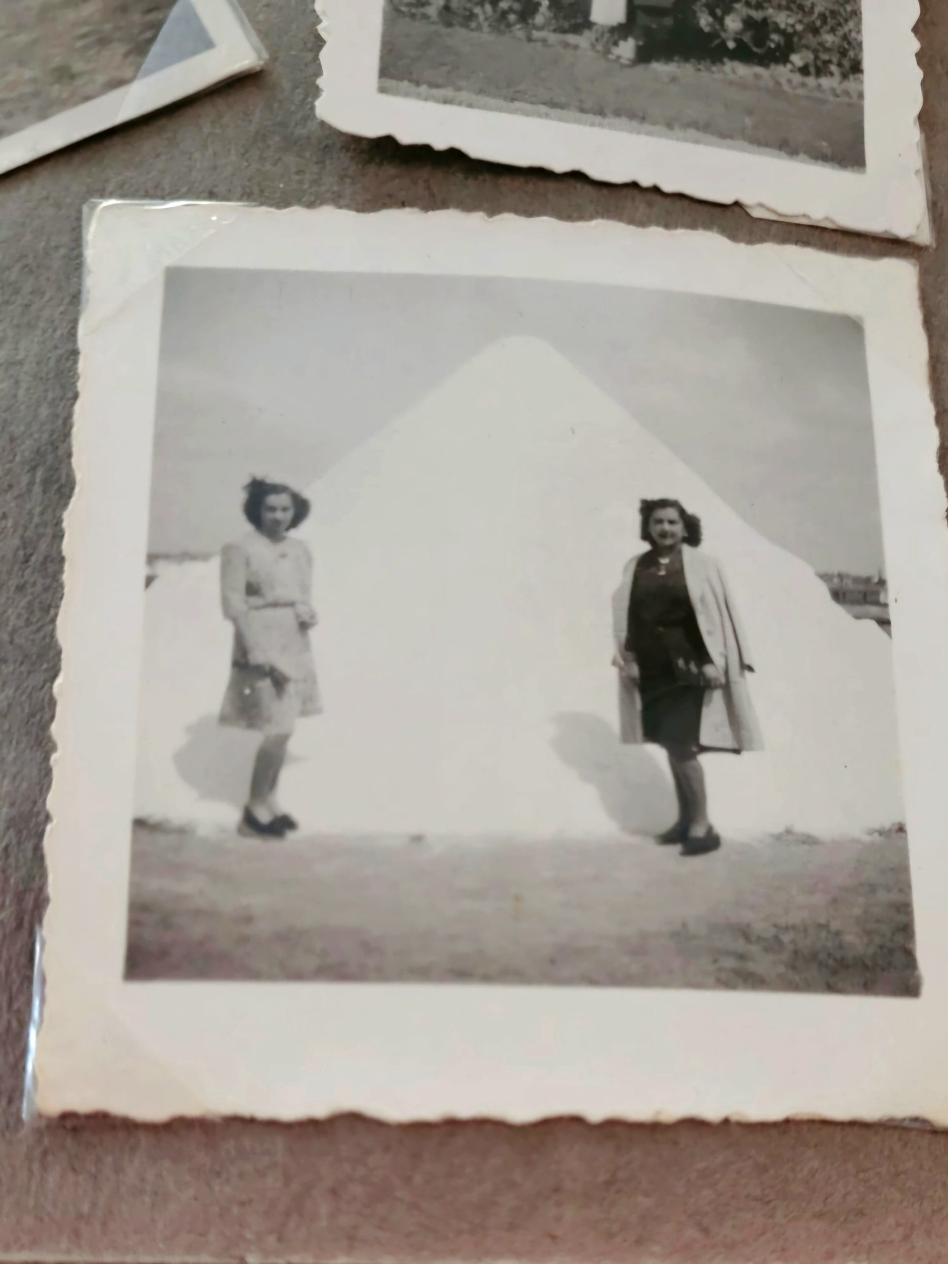 Vintage black-and-white photograph showing two women standing outdoors beside a large pale mound, possibly snow or sand. 