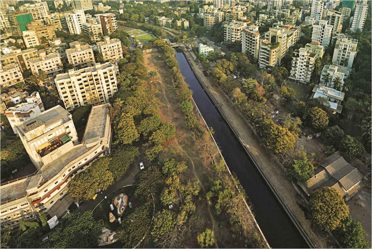 Aerial photo of a dense urban neighborhood with numerous high-rise residential buildings surrounding a long, tree-lined dark corridor. 